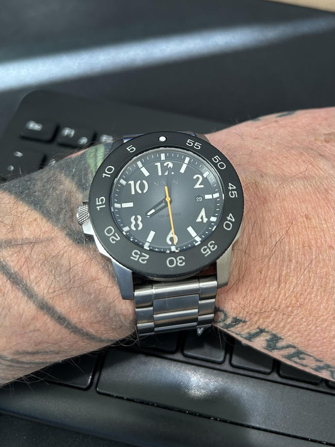 Man sitting at a keyboard and showing off his Nixon Smyth 44 analog watch