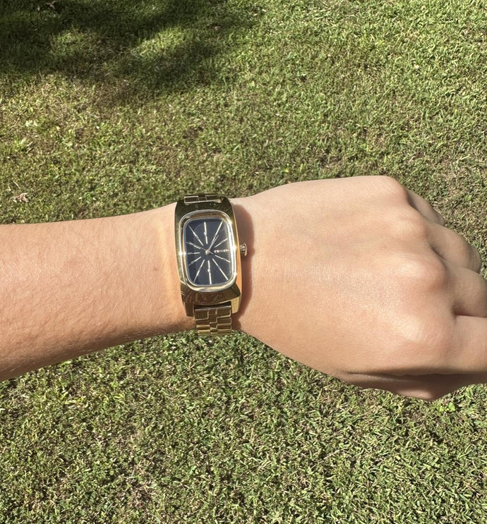 Wrist wearing a gold Nixon Frankie analog watch while outdoors